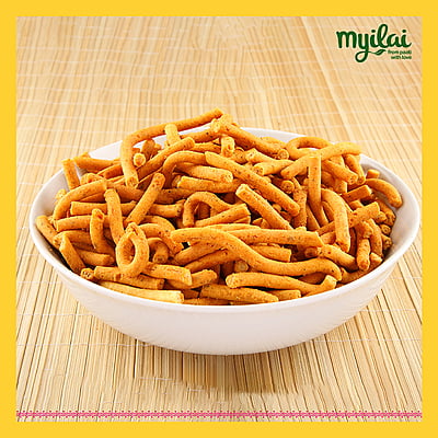 A bowl of Millet Kara Sev is placed on a wooden table with myilai logo on top